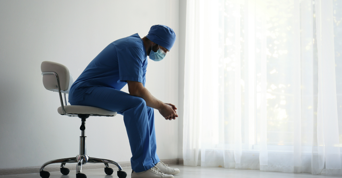 An exhausted doctor leans over in a chair. 